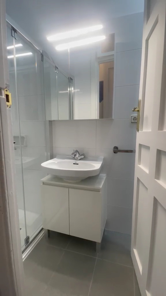 Baño reformado con mampara de ducha, lavabo y mueble blanco