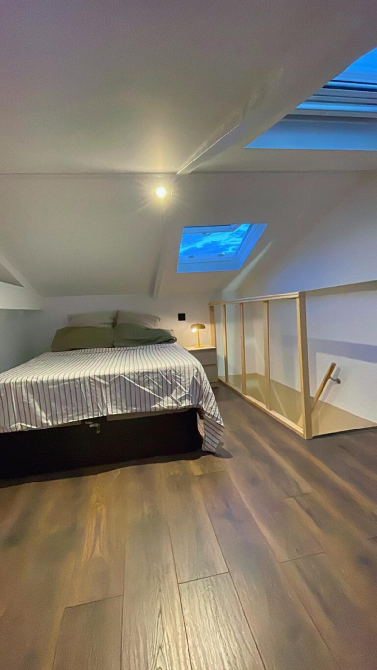 Dormitorio abuhardillado reformado con ventana de tejado y barandilla de madera