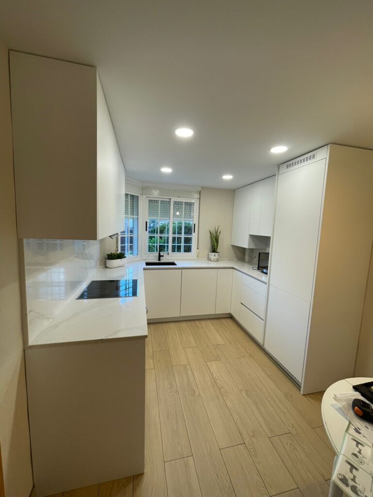 Cocina lineal reformada con muebles blancos y suelo imitación madera