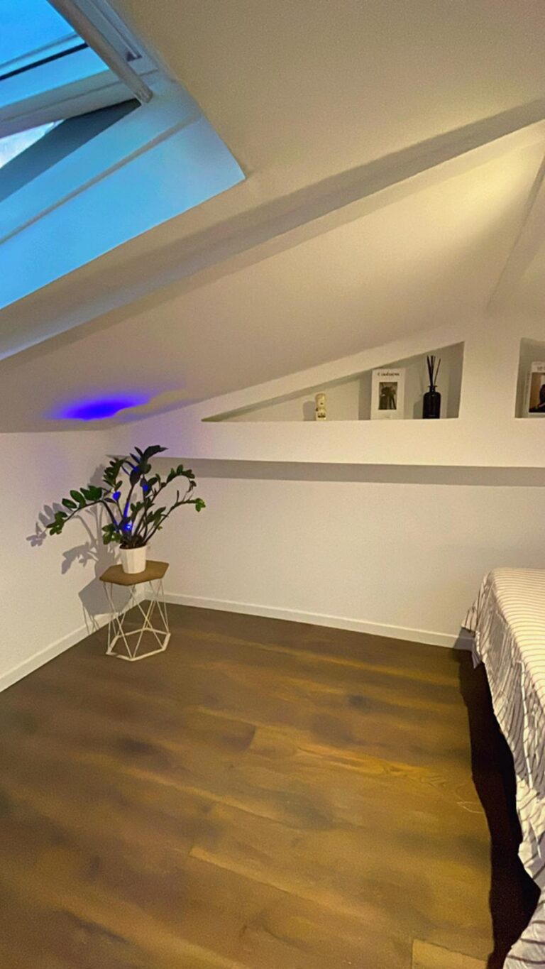 Dormitorio abuhardillado reformado con suelo laminado y paredes blancas