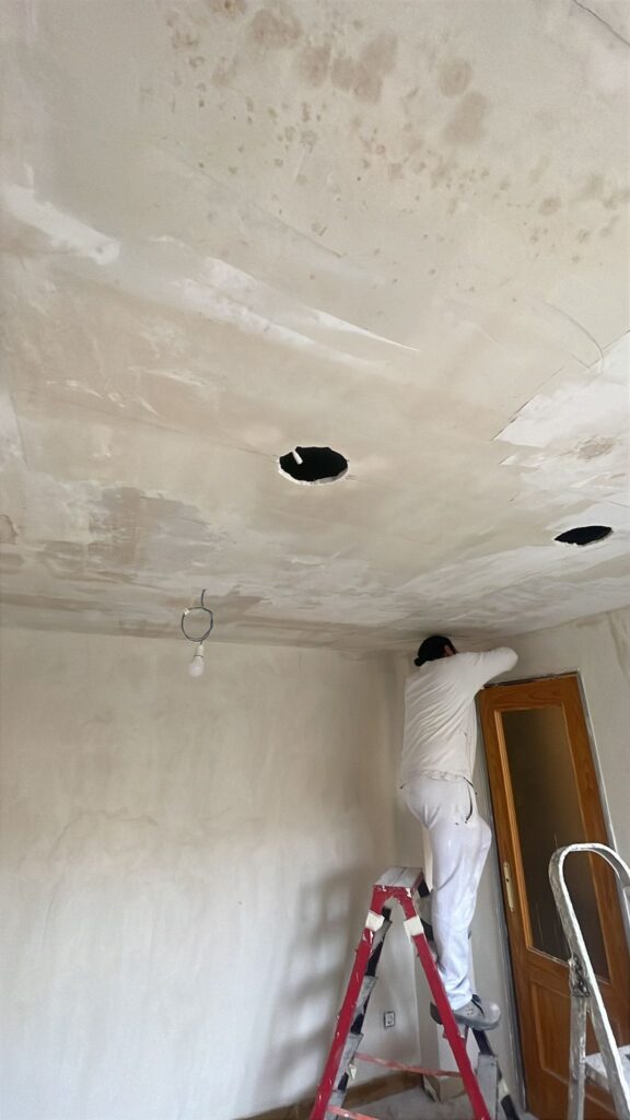 Operario preparando y pintando el techo de una vivienda en obra